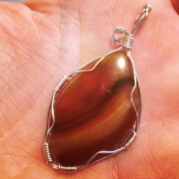 Brown and tan striped teardrop pendant in silver wire, resting on a hand