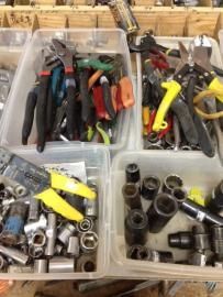Plastic bins of assorted hand tools and sockets, including pliers, screwdrivers, and wrenches, on a workbench.