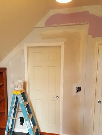 A blue ladder is sitting next to a white door in a room.