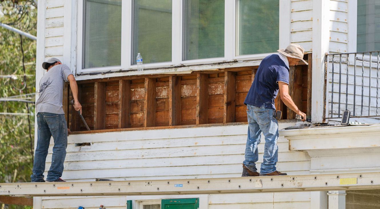 Two men are working on the side of a house.