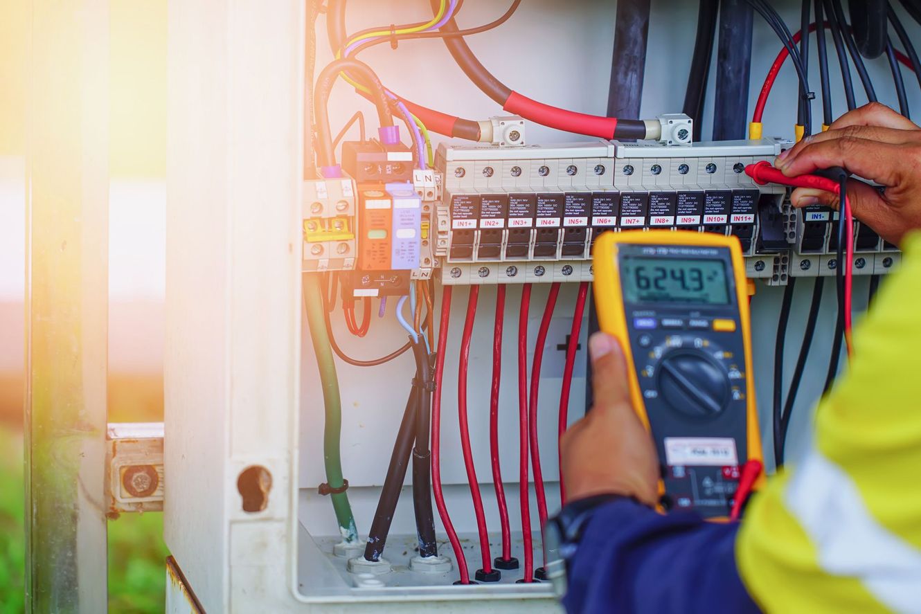 An electrician is using a multimeter to test an electrical box.