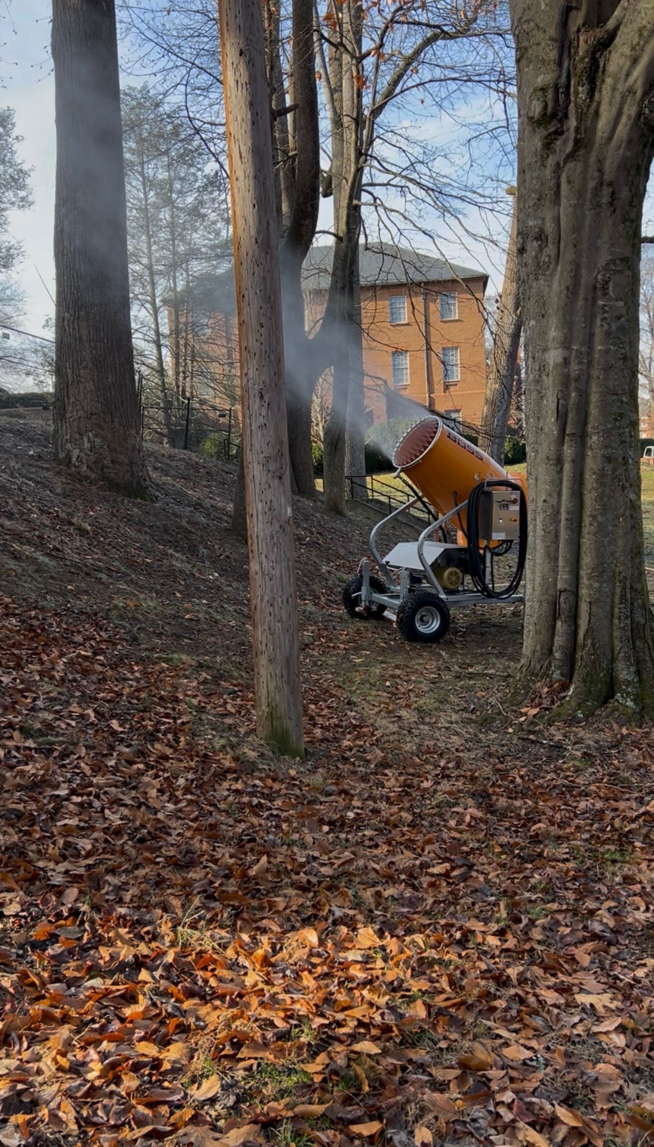 A machine spraying mist among trees in a wooded area near a building.