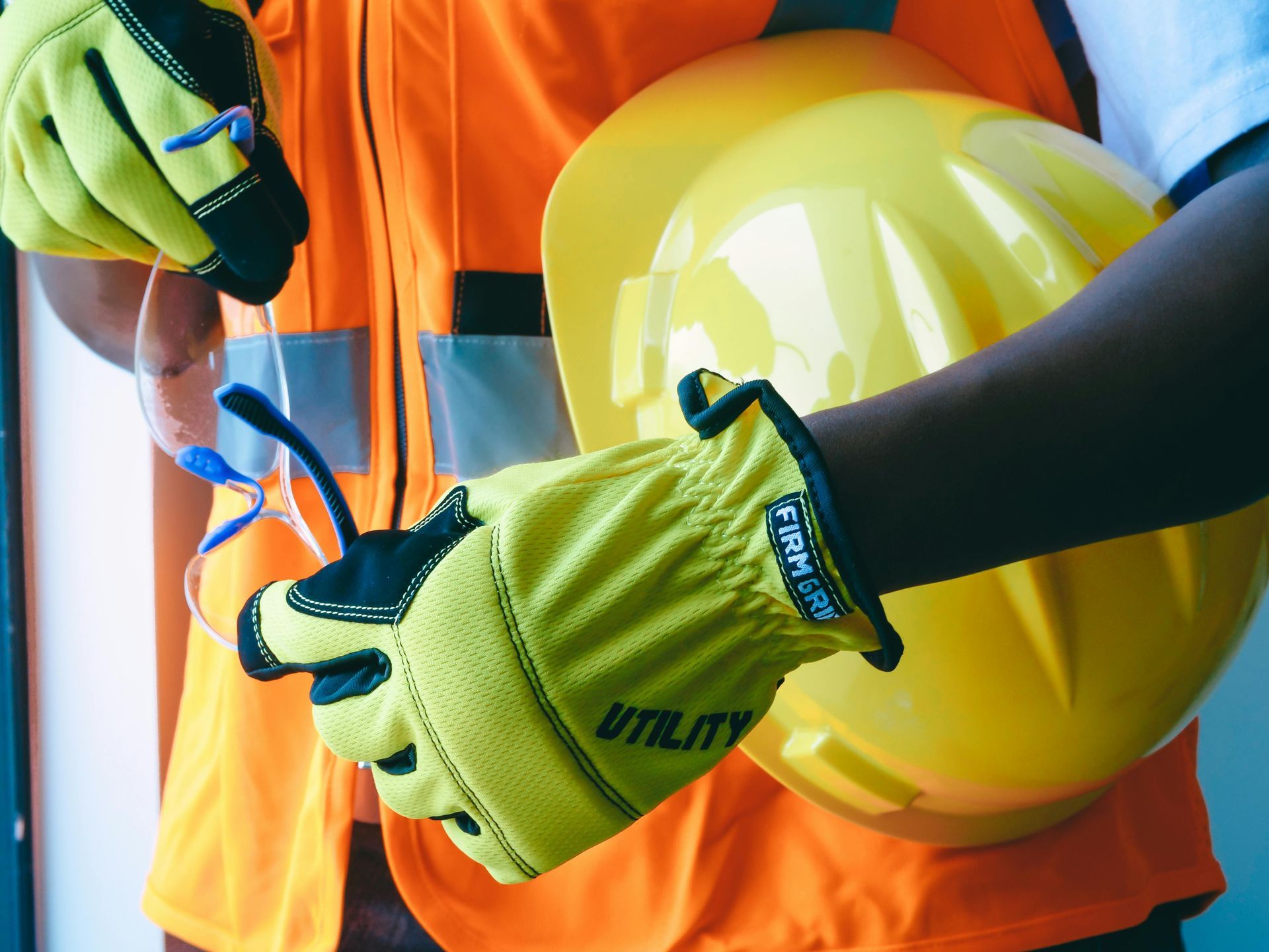 Construction worker in orange vest holding yellow hard hat and using blue pliers
