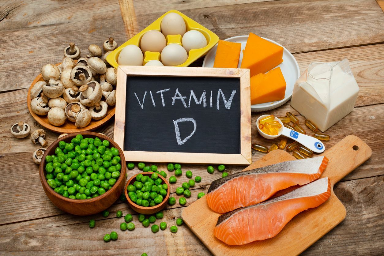 Foods high in vitamin D arranged on a wooden surface: eggs, salmon, cheese, mushrooms, and peas.