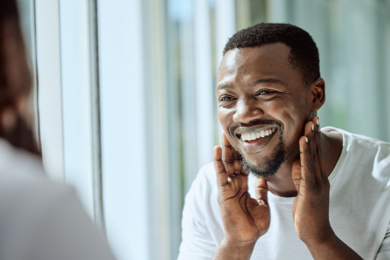 A man is smiling while looking at his face in the mirror.