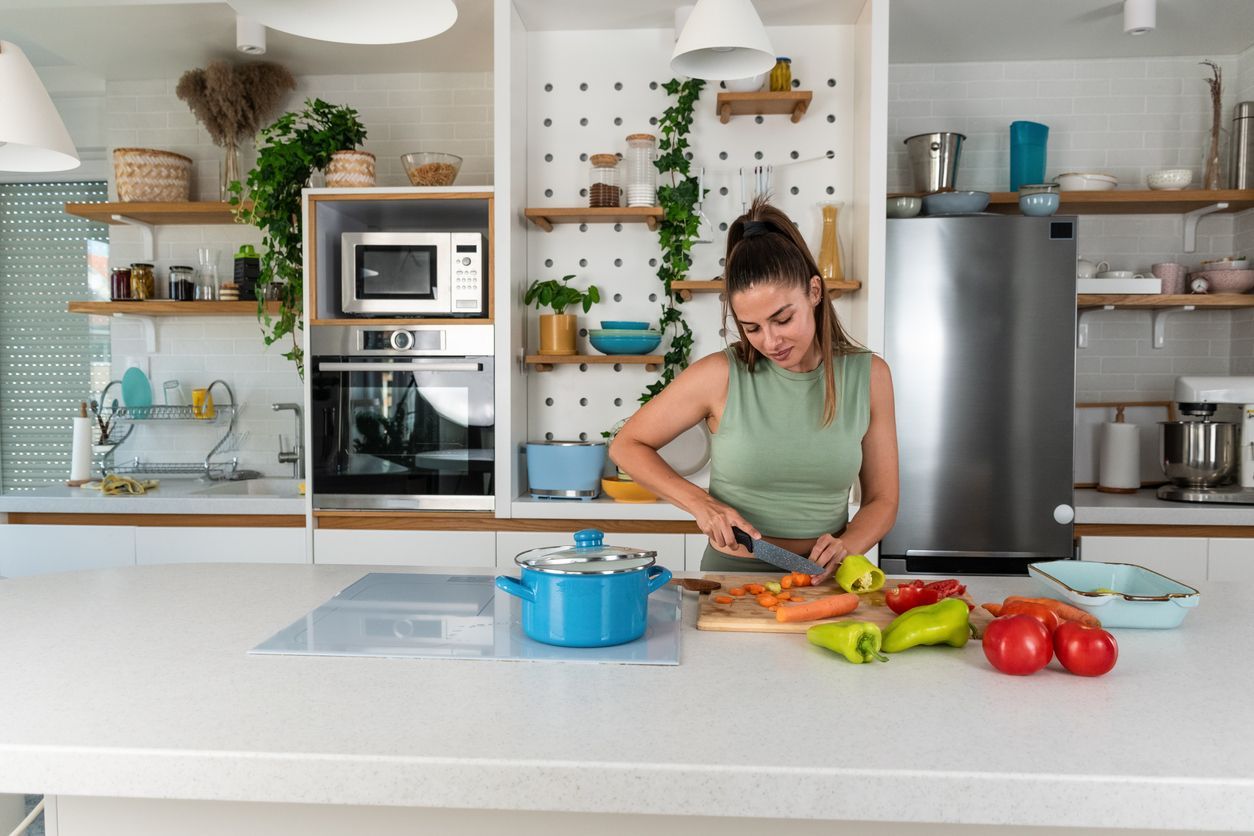 Woman in a green top chopping vegetables in a bright white kitchen with a blue pot on the counter.