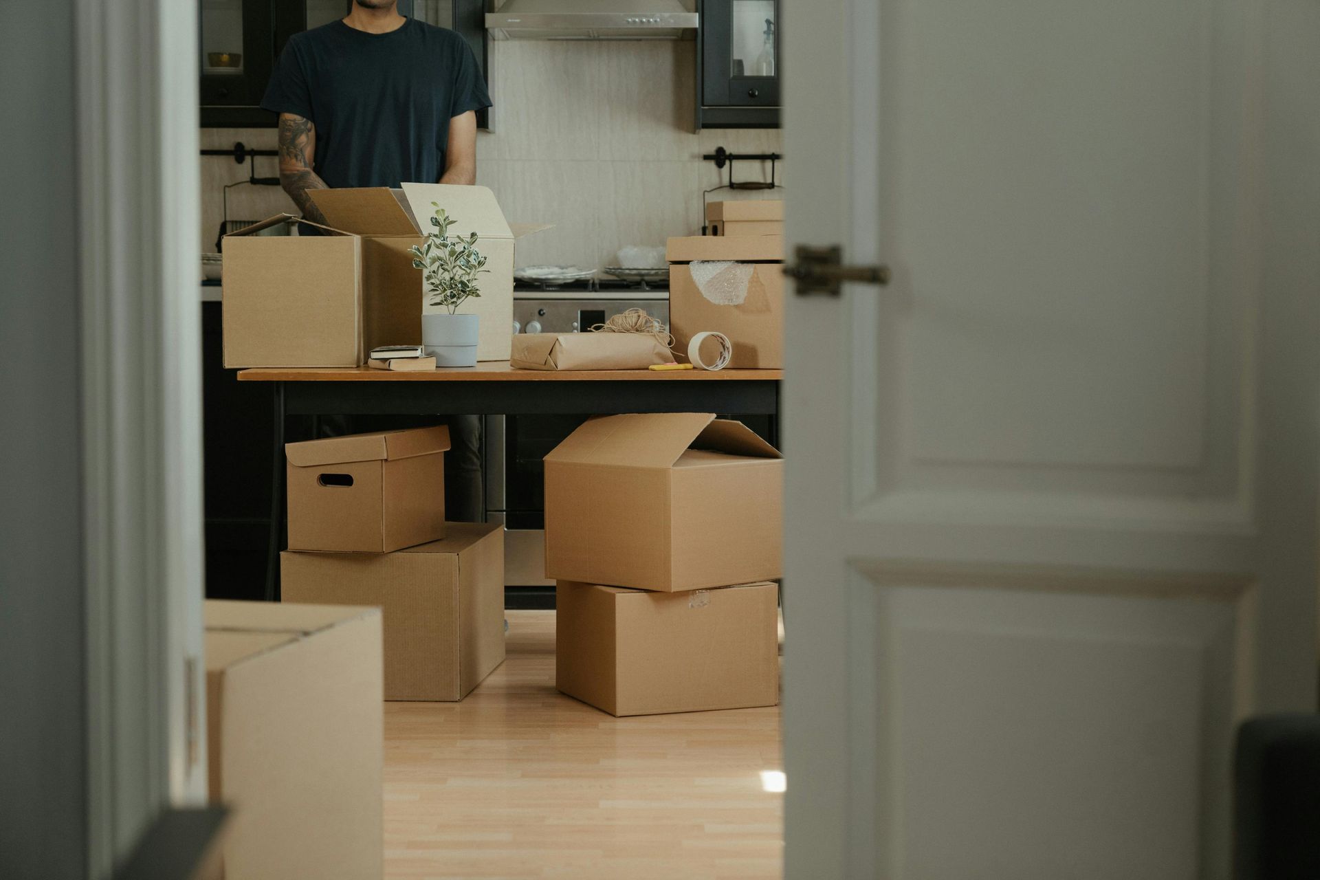 A person in a kitchen surrounded by cardboard boxes, packing items during a move.