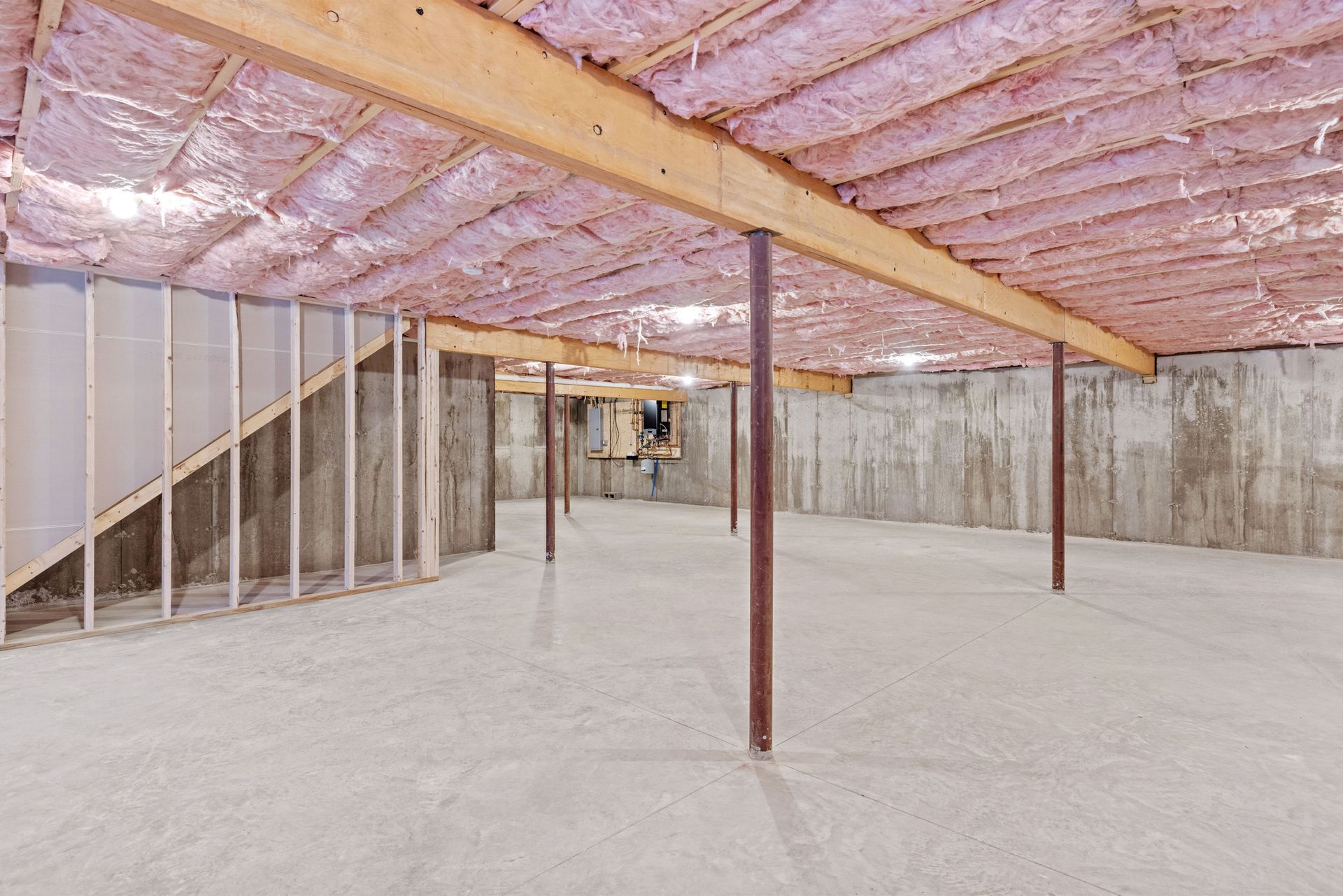 An empty basement with insulation on the ceiling and walls.