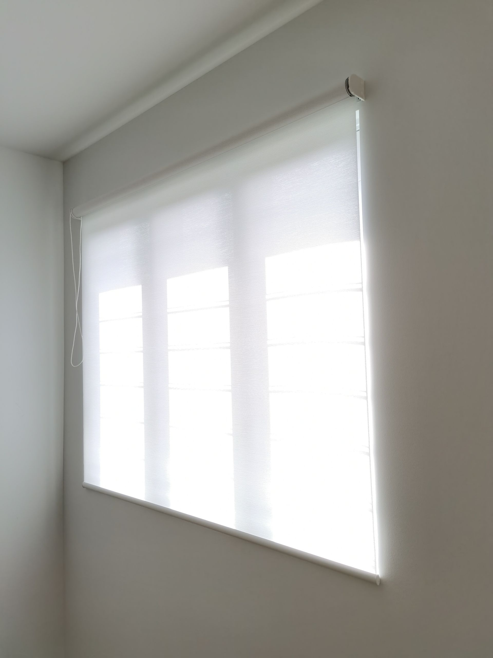 A white roller blind is hanging on a window in a room.