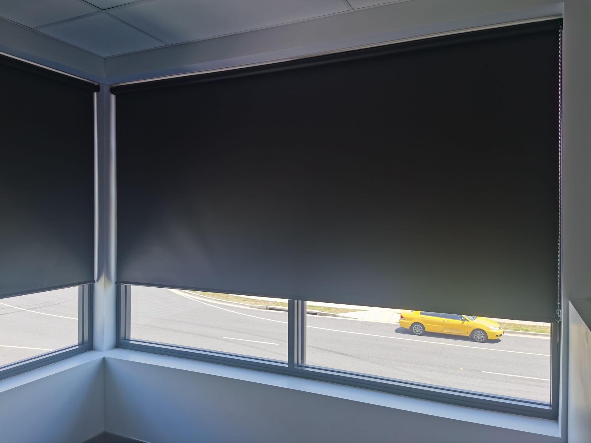 A yellow car is driving down the street through a window with black blinds.