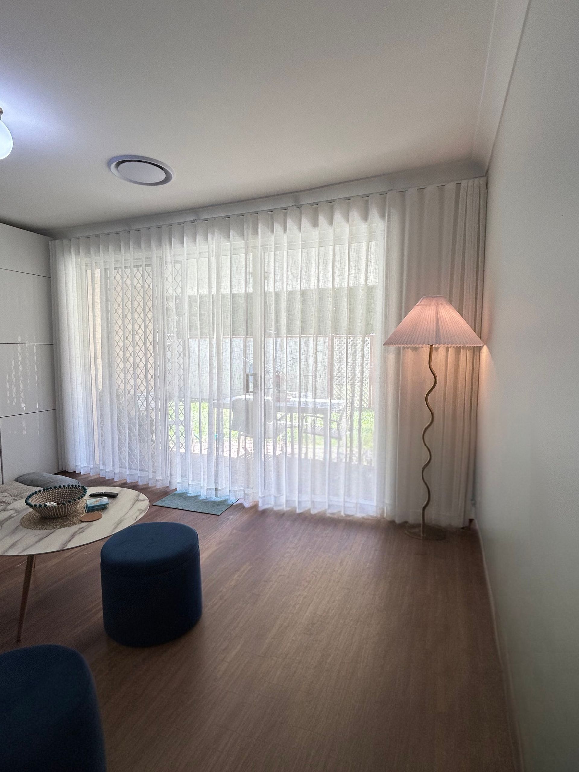 A living room with a table , ottoman , lamp and sliding glass doors.