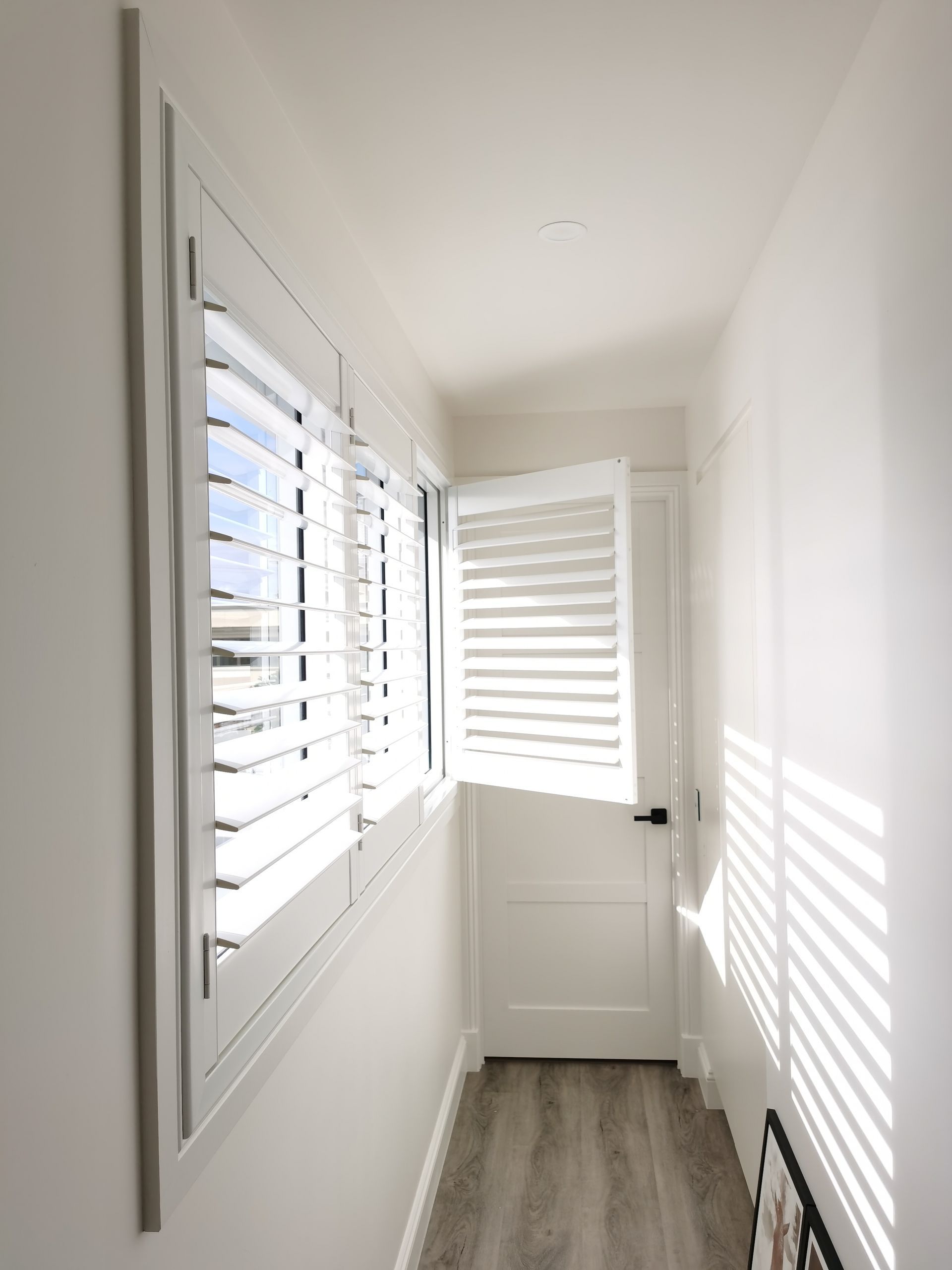 A hallway with white shutters on the windows and a door.