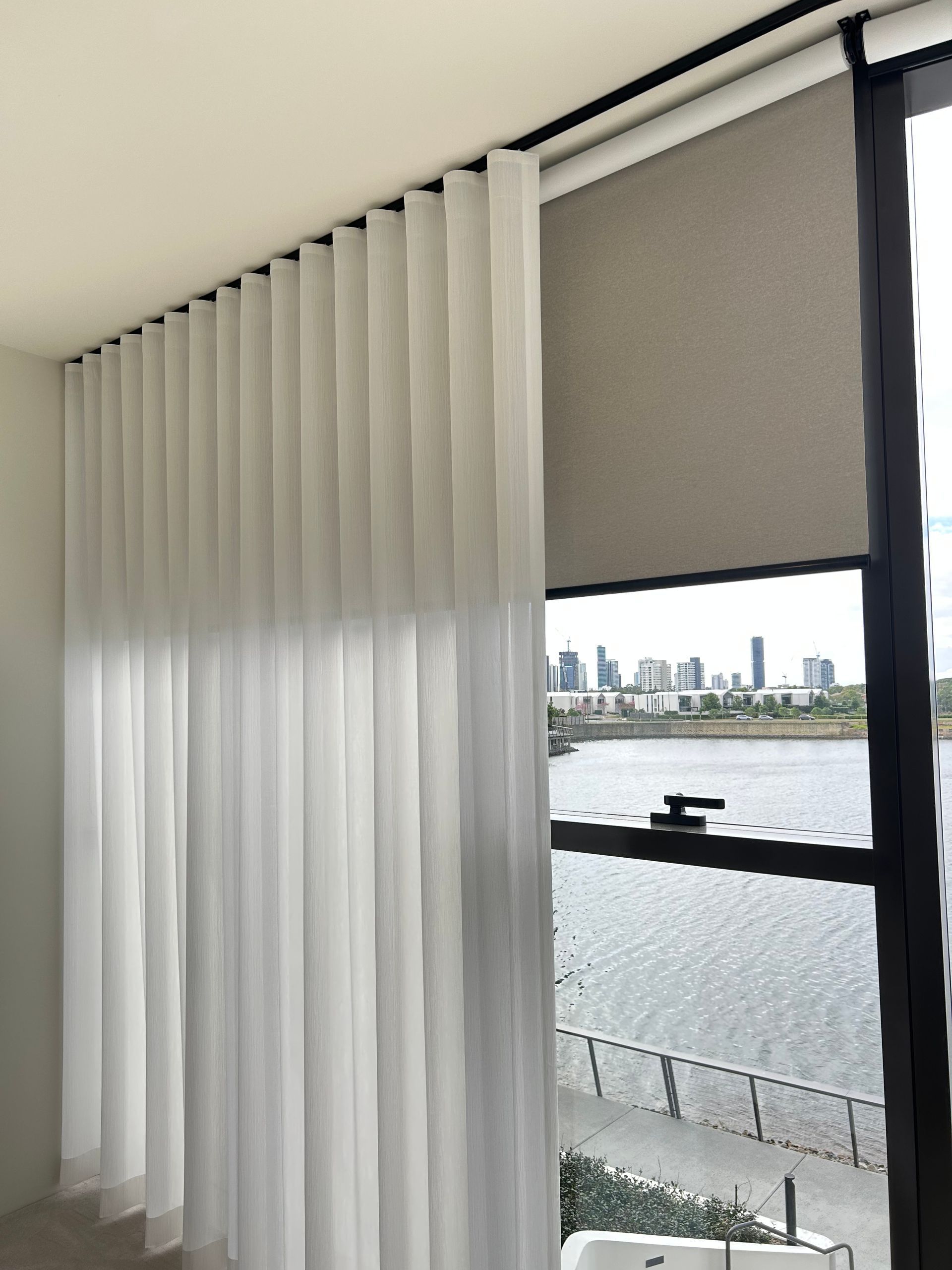A room with white curtains and a large window with a view of the water.