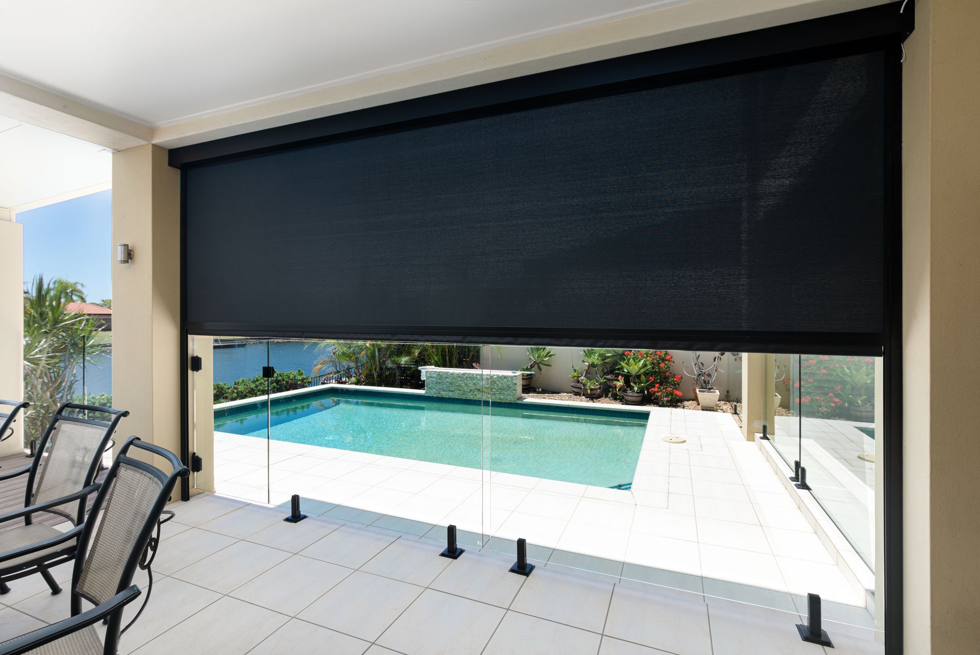 A patio with a swimming pool in the background and a black awning over it.