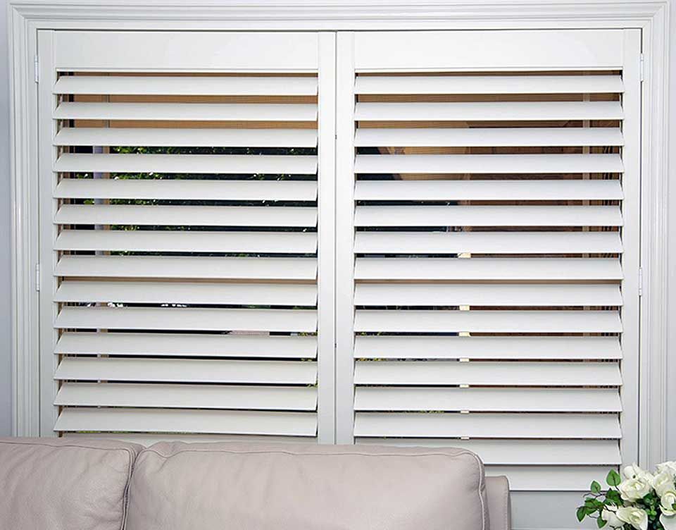 A living room with a couch and a window with white shutters