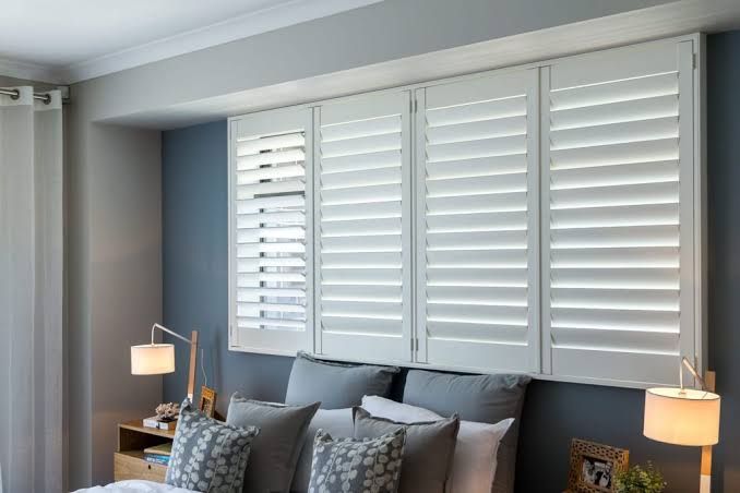 A bedroom with a bed , lamps and shutters on the wall.