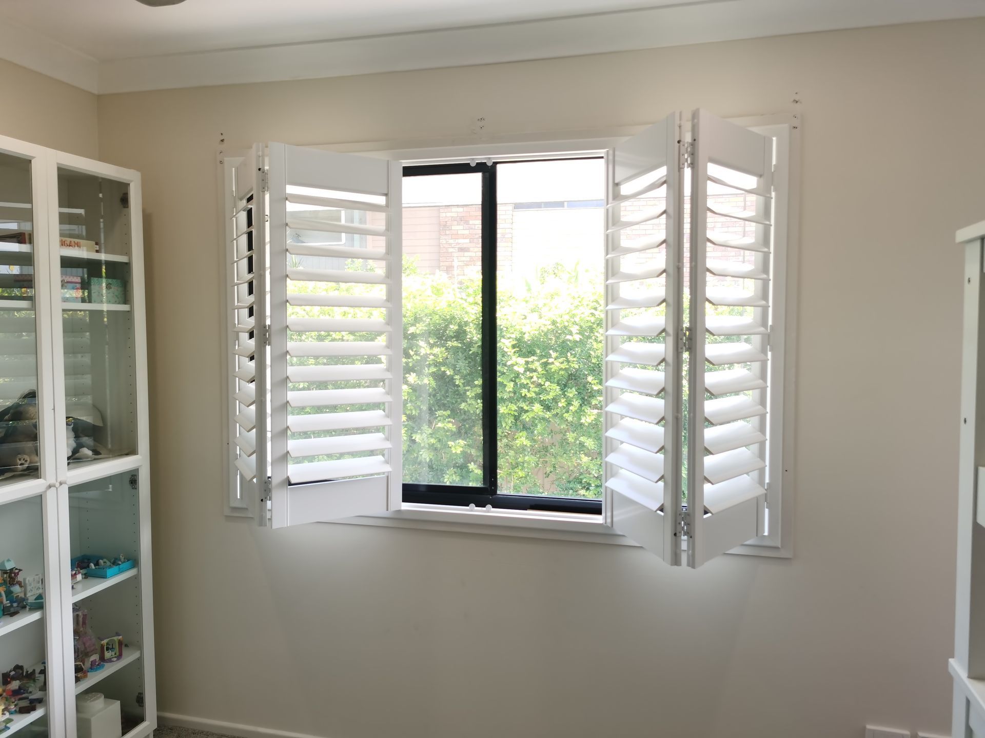 A room with a window and white shutters on it.