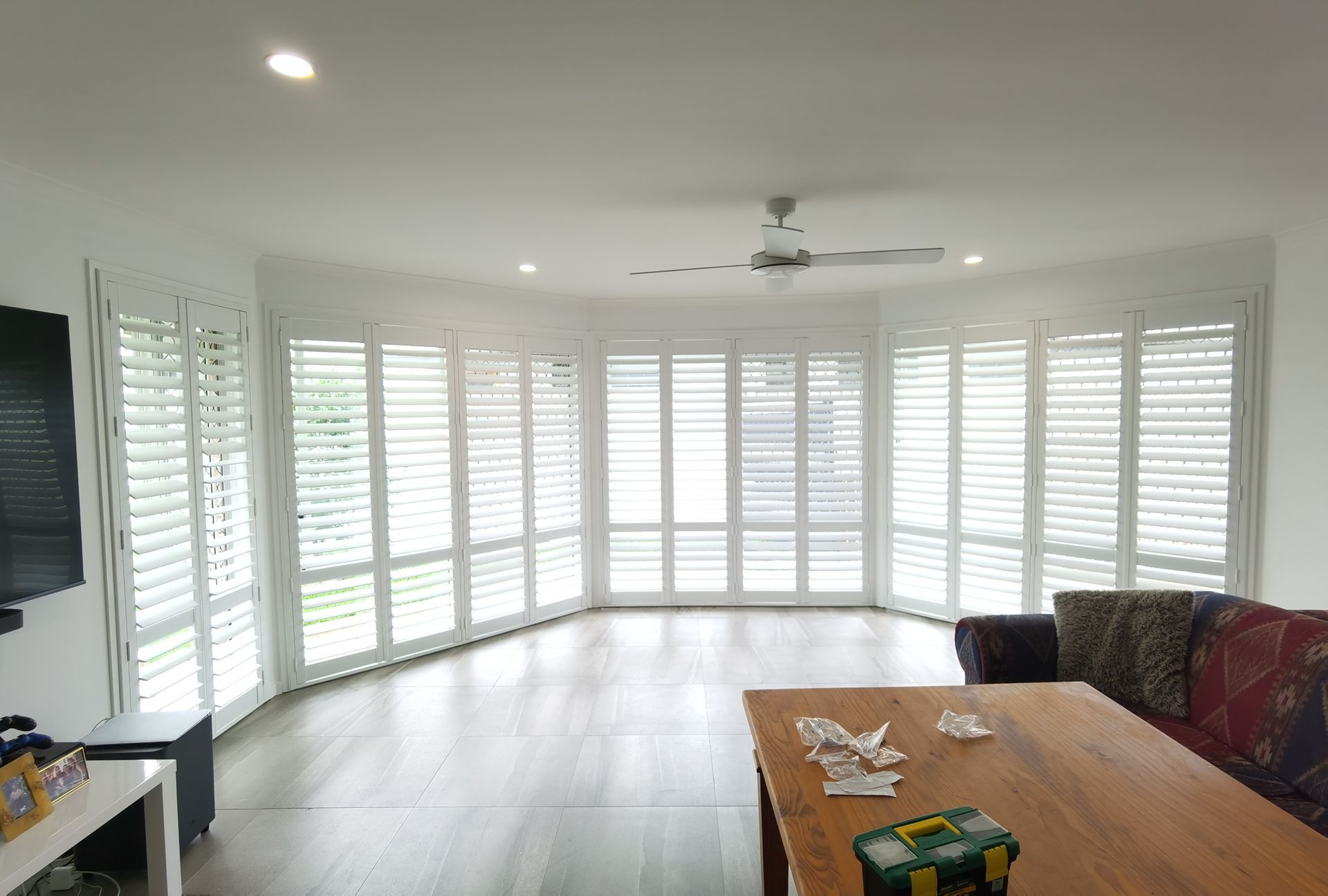 A living room with a couch , table , television and shutters on the windows.