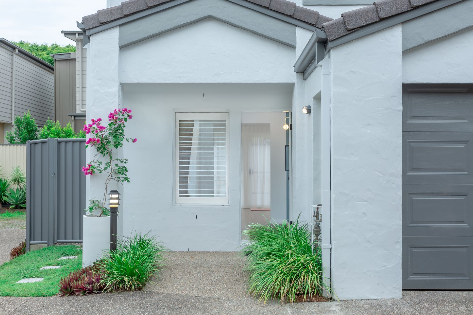 A white house with a gray garage door and a purple flower in front of it.