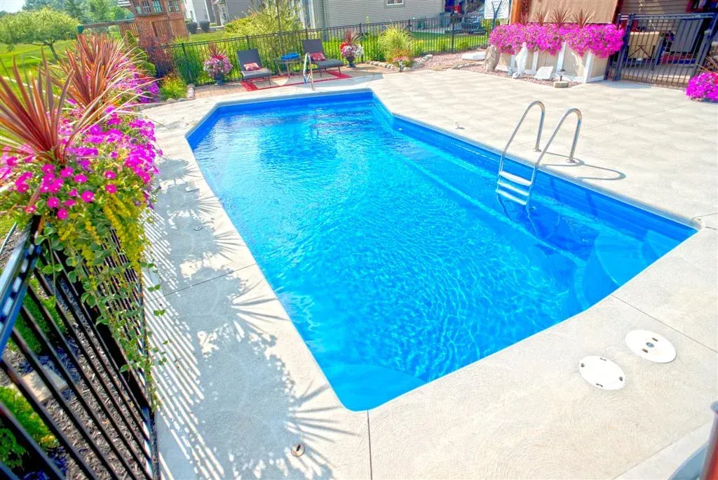 A large blue swimming pool is surrounded by flowers and a fence.