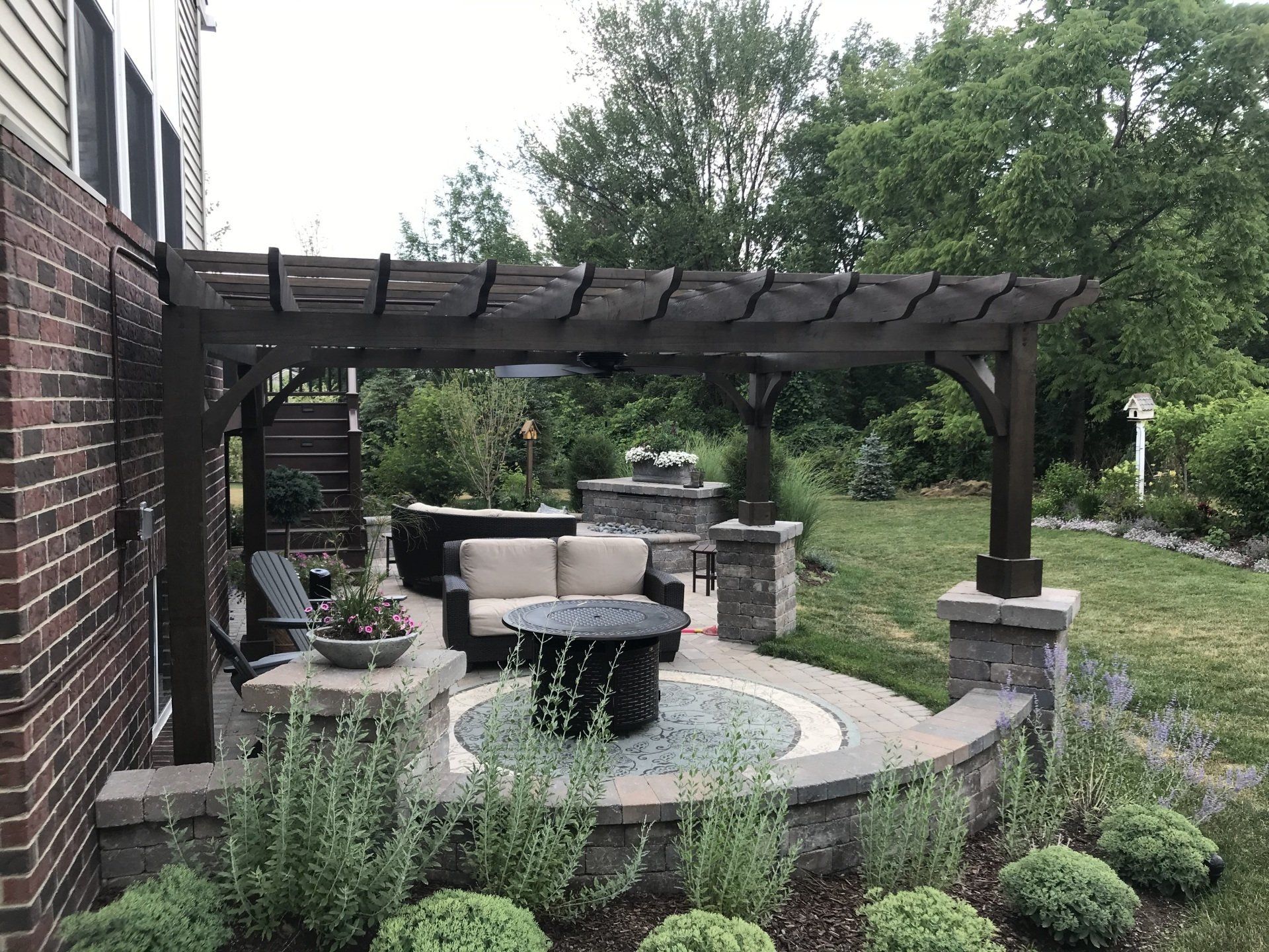 A patio with a pergola and a fire pit in the backyard of a house.