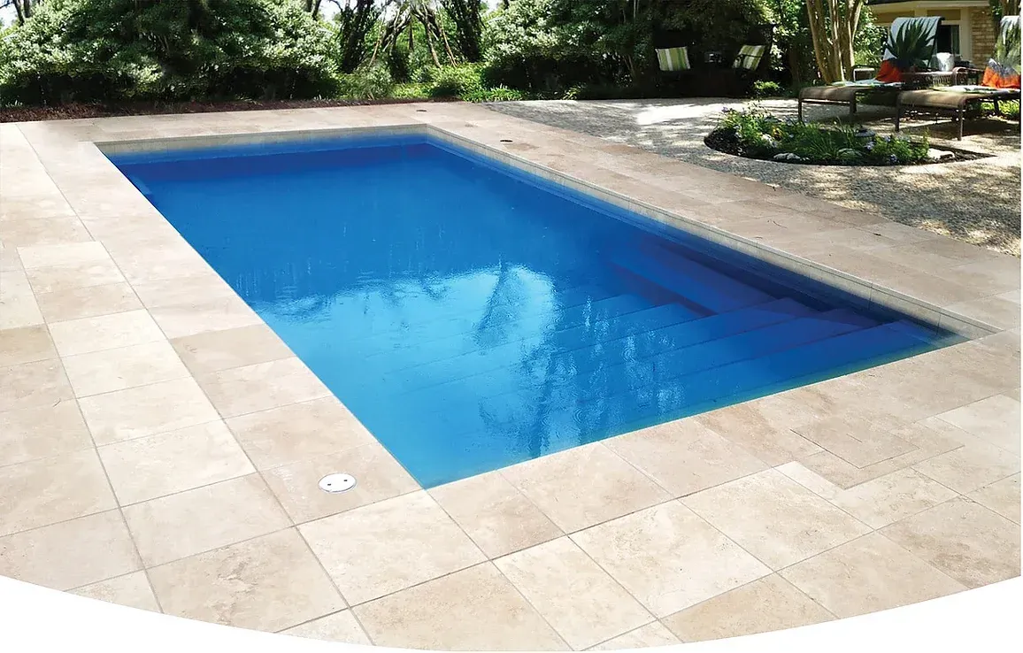 A large swimming pool is surrounded by tiles and trees