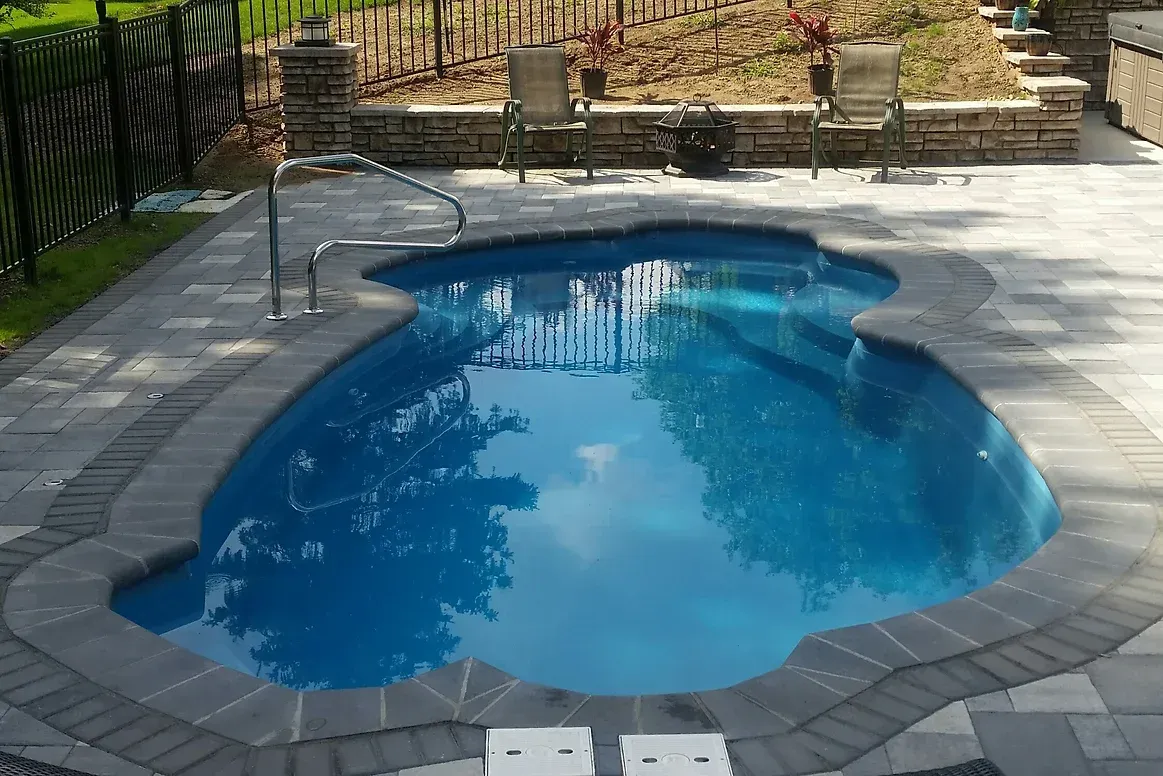 A heart shaped swimming pool is surrounded by a patio and chairs.