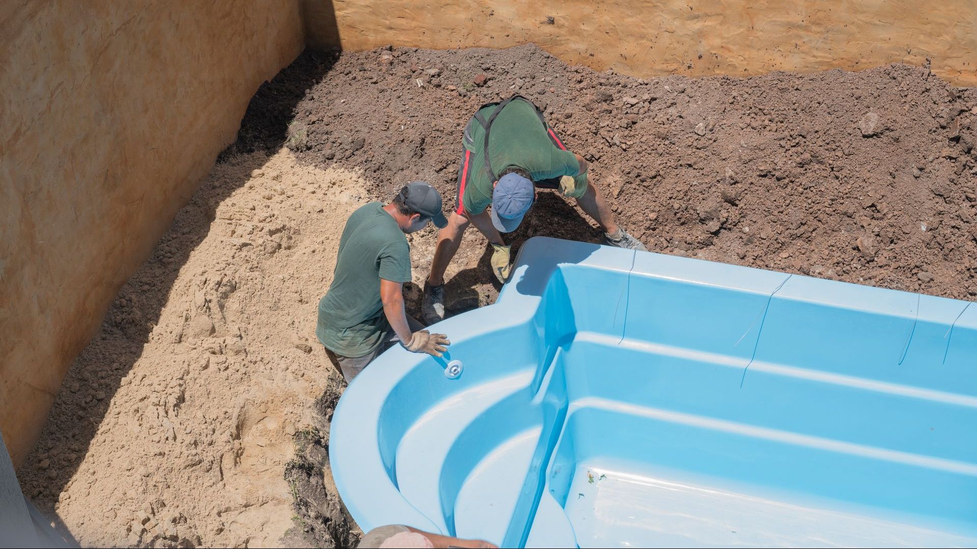 Two men are working on a blue swimming pool.