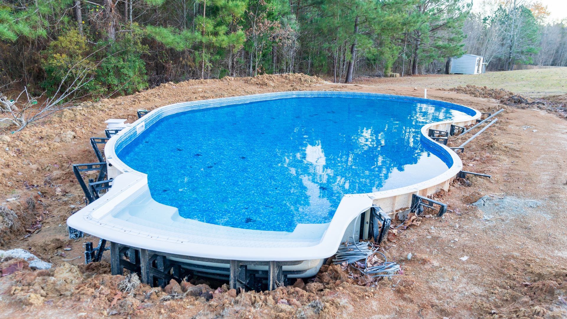 A large swimming pool is sitting in the middle of a dirt field.