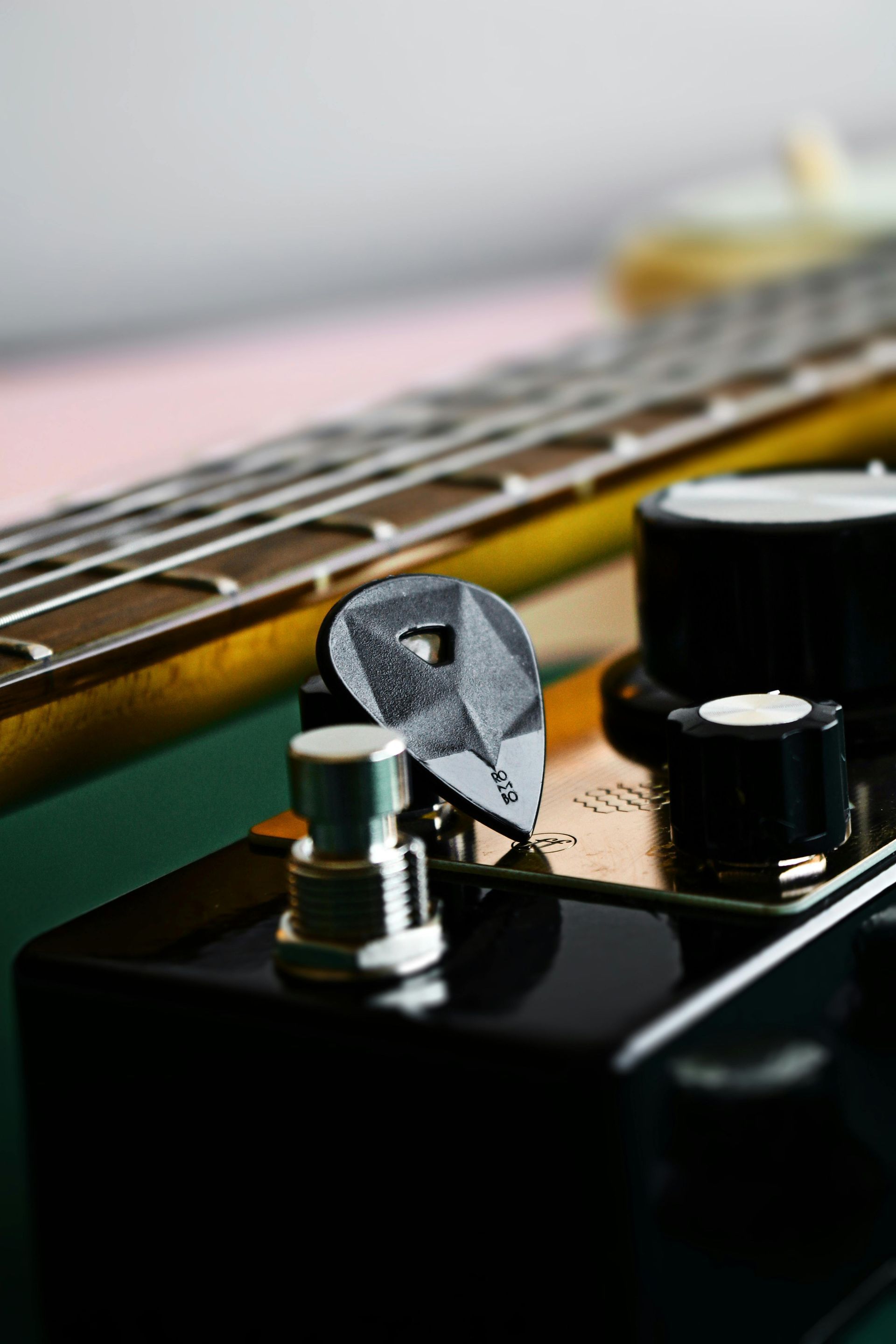 Close-up of a black guitar, pick on the body near the neck, with black knobs and chrome pedal.