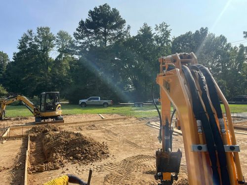 Excavators at a sunny construction site, with one machine in the foreground and dirt piles nearby.
