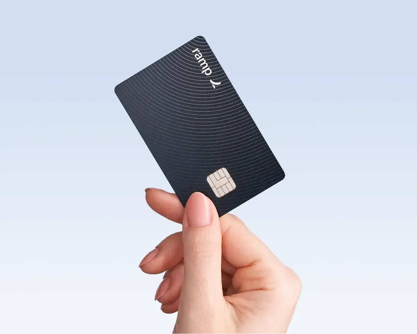 Hand holding a black Ramp credit card against a light blue background.