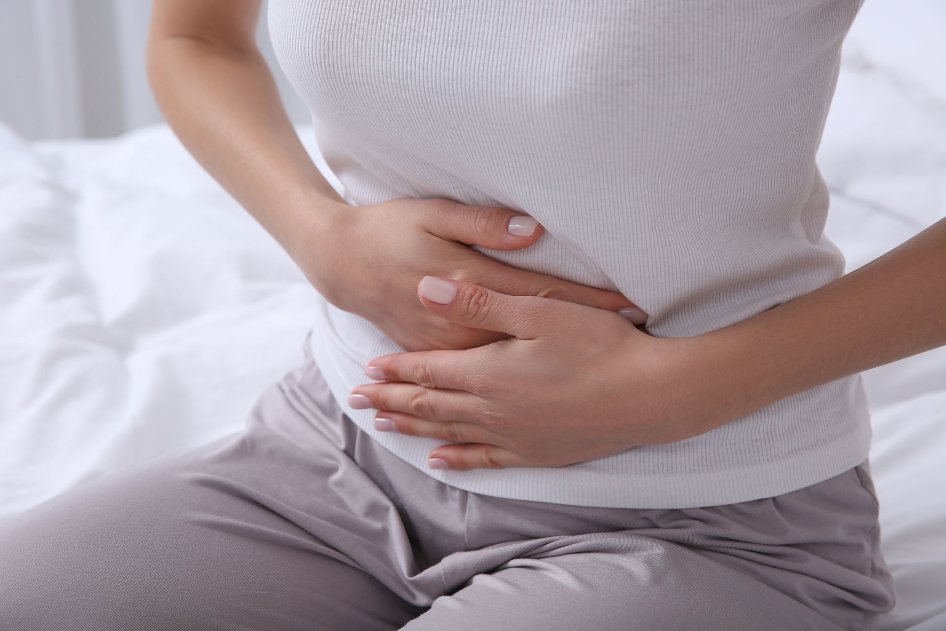 Person holding their lower abdomen on a bed, suggesting stomach pain. Person holding their lower abdomen on a bed, suggesting stomach pain.