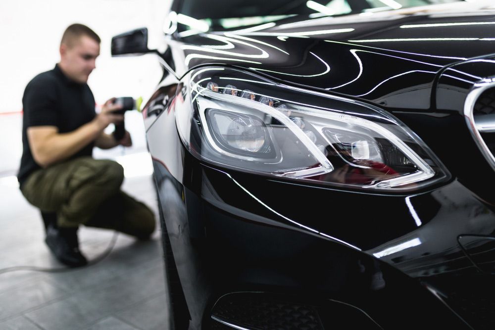 A Man is Polishing the Headlights of a Black Car — Shane’s Car Detailing & Office Cleaning in Gunnedah, NSW