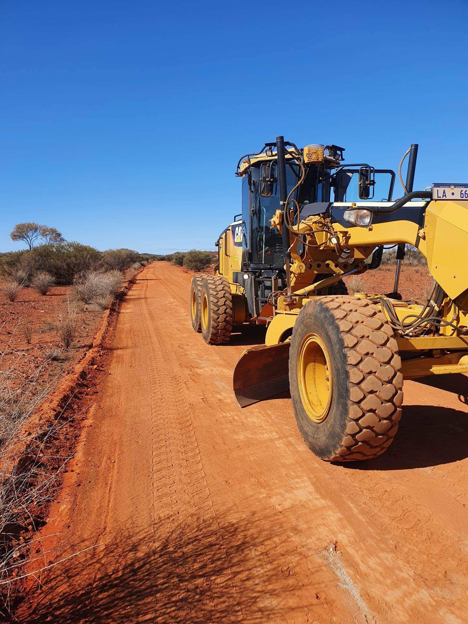A yellow tractor is driving down a dirt road.