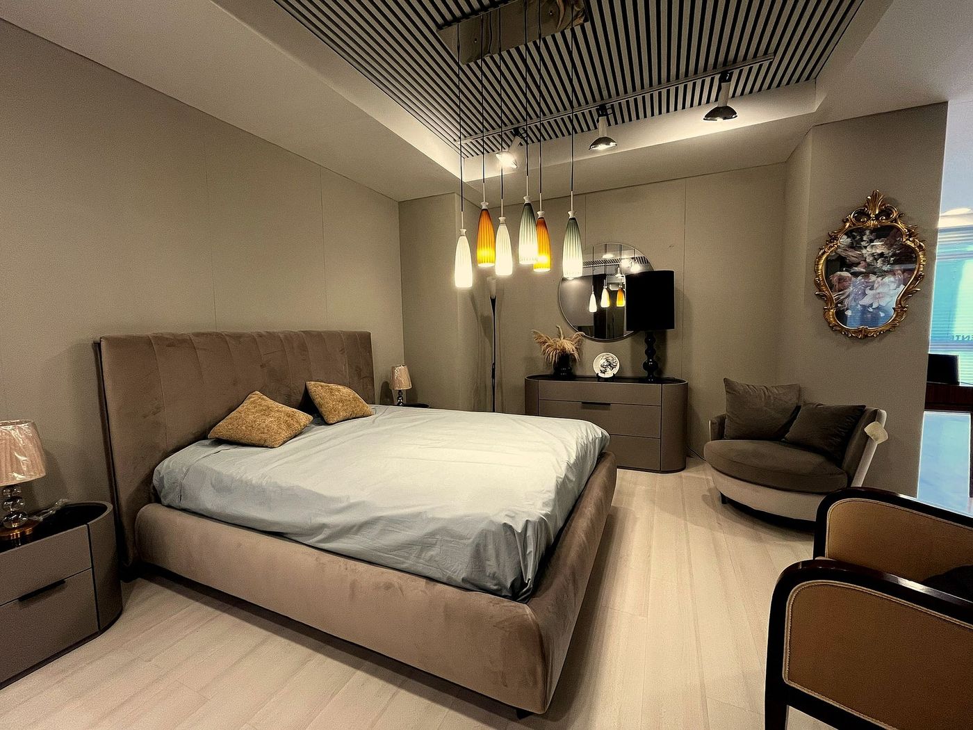 Camera da letto moderna con letto beige, lampade a sospensione, comò, sedia e specchi decorativi.