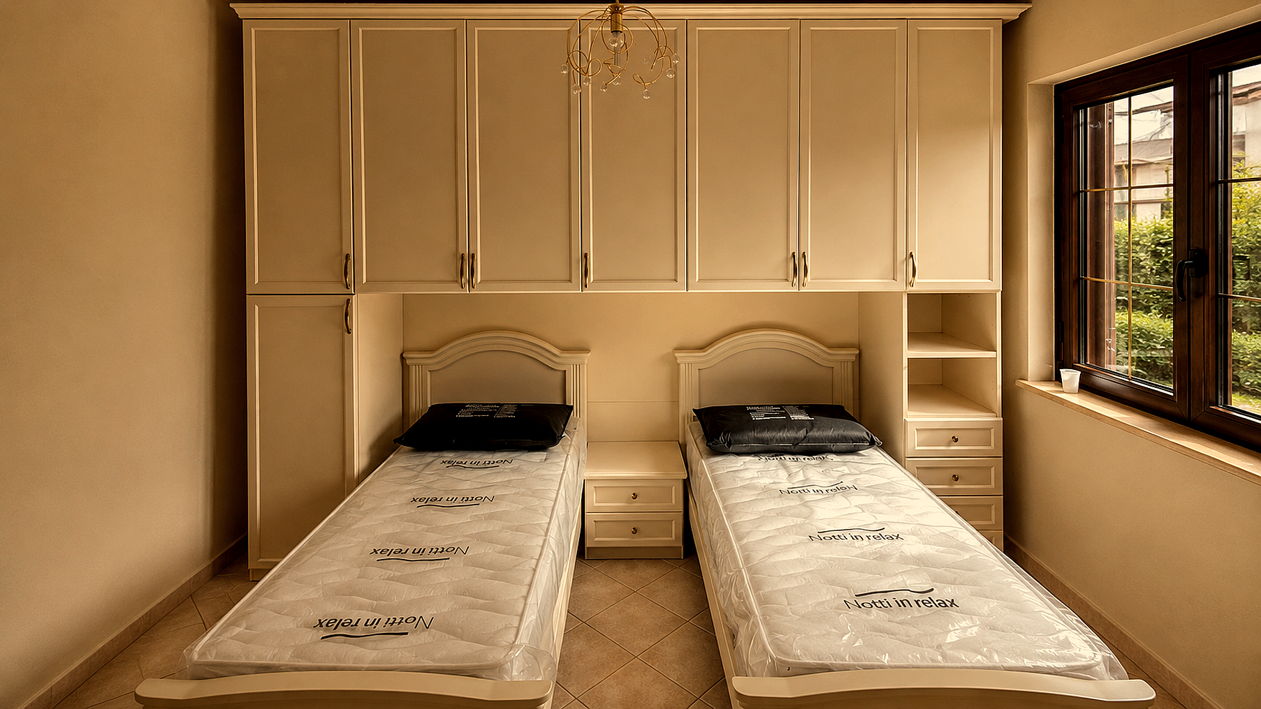 Piccola camera da letto con due letti singoli, armadi a muro color crema e una finestra sulla destra.