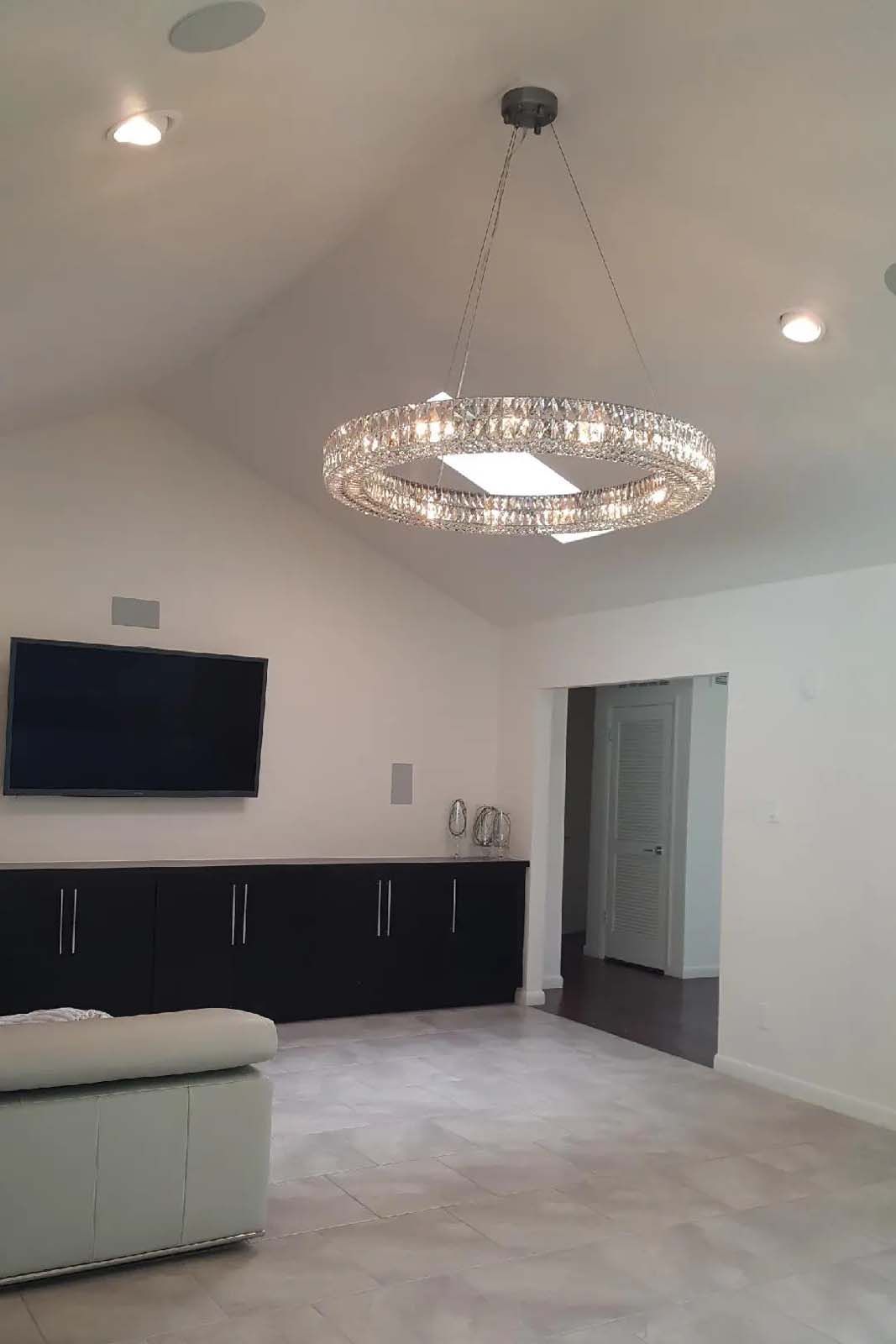 A living room with a chandelier hanging from the ceiling and a flat screen tv.
