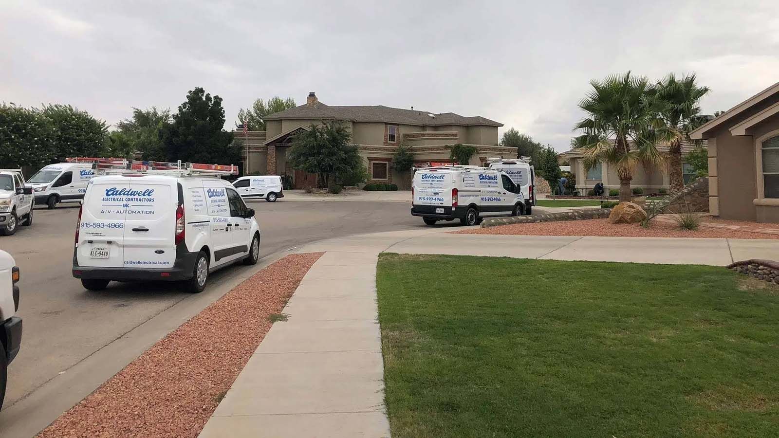 A bunch of vans are parked on the side of the road in front of a house.