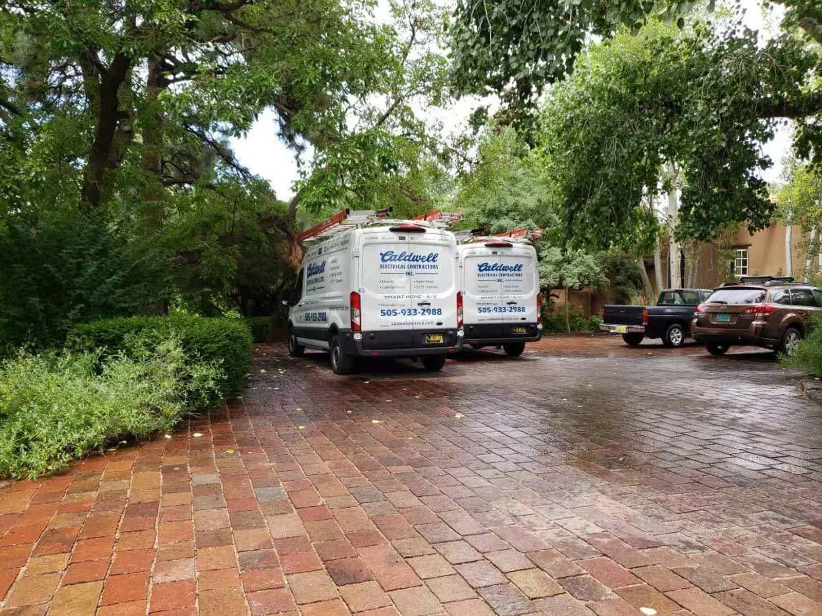 Two white vans are parked on a brick driveway.