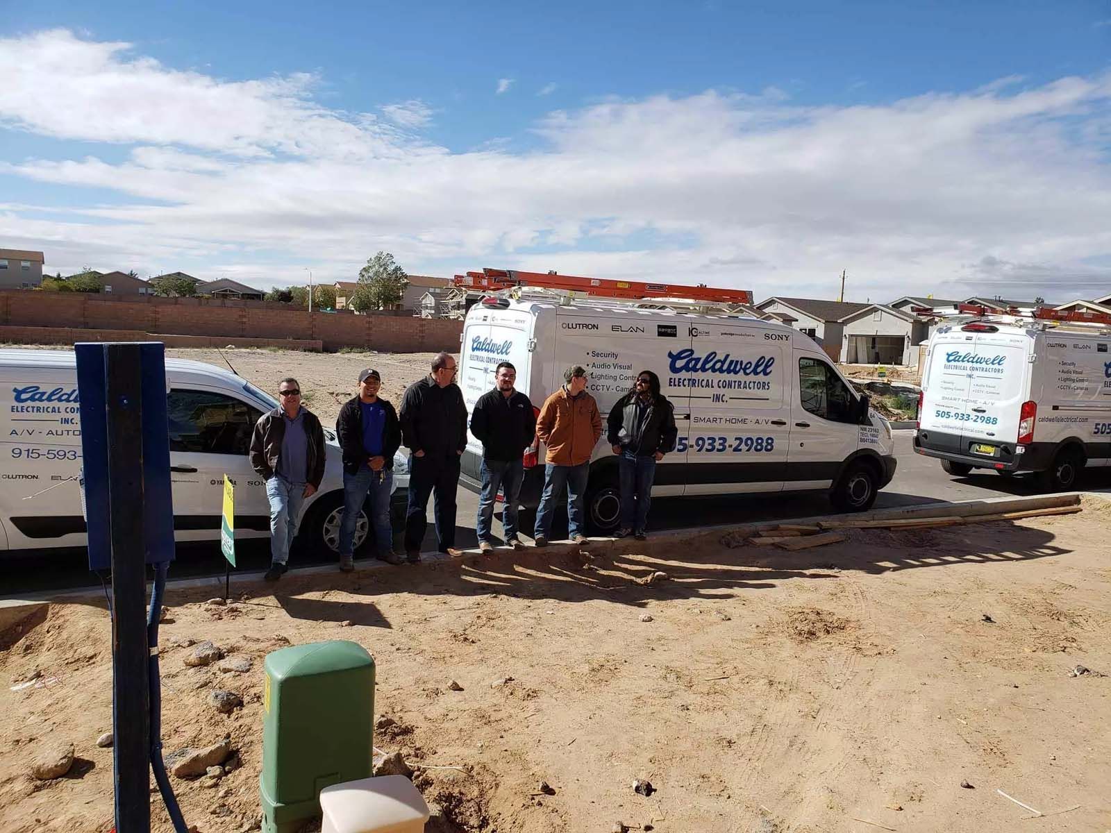 A group of men are posing for a picture in front of a row of vans.