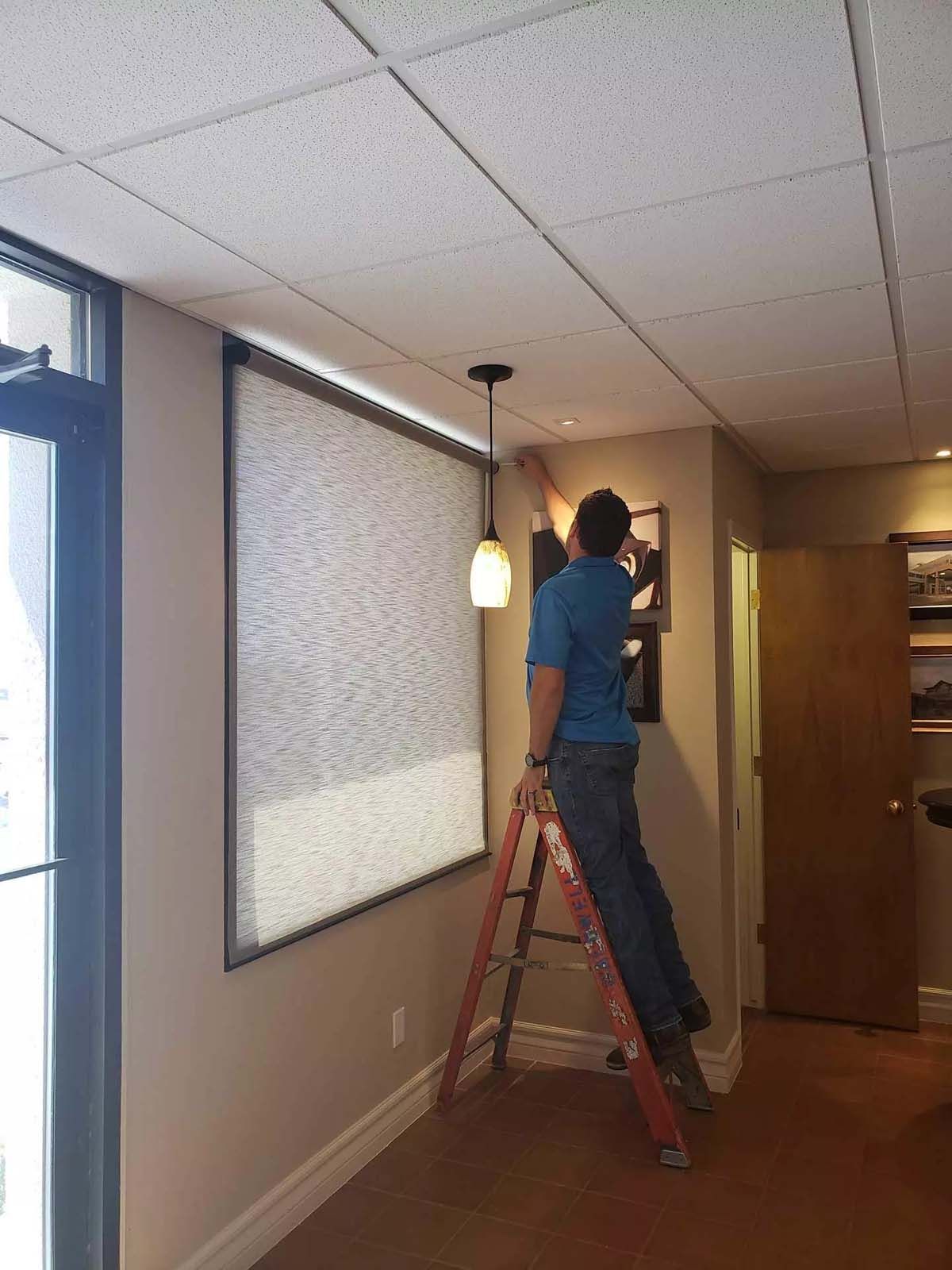 A man is standing on a ladder in front of a window.