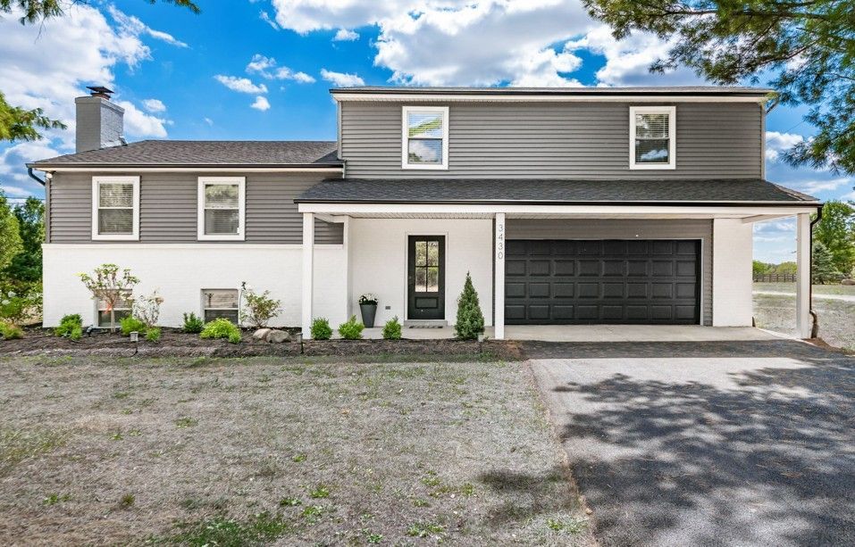 Two-story house with gray siding and white trim. Black garage door, driveway. Blue sky, green yard. Two-story house with gray siding and white trim. Black garage door, driveway. Blue sky, green yard.