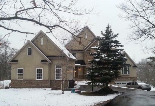 Two-story house in winter, beige siding with brick, snow on the ground, evergreen tree, and a truck in the driveway.