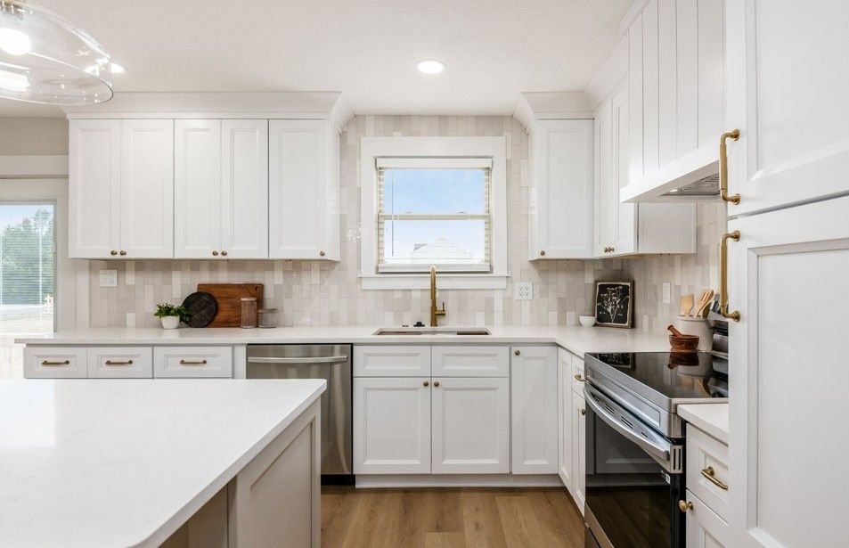Bright, modern kitchen with white cabinets, stainless steel appliances, and a large island. Includes wooden floors and brass hardware.