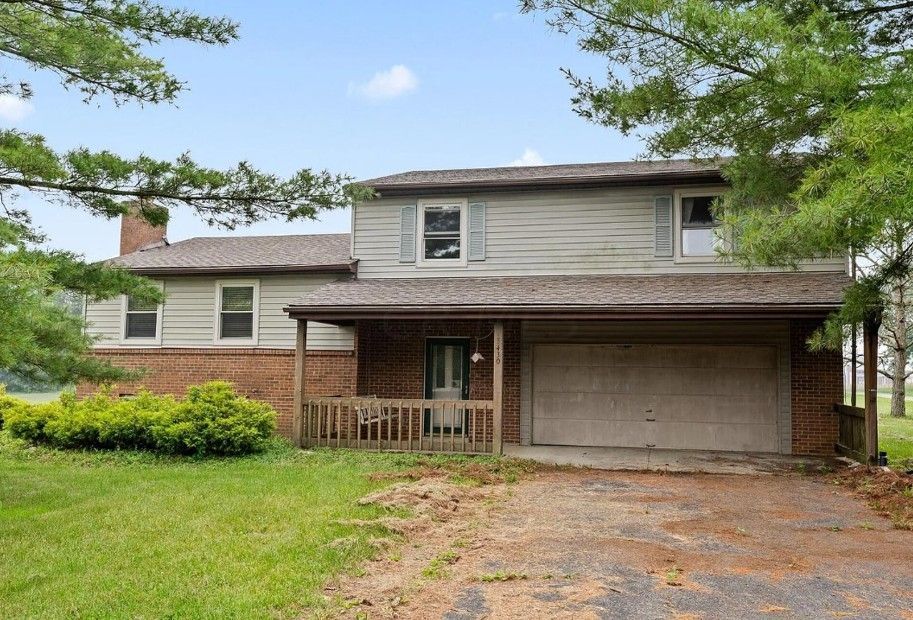 Two-story house with gray siding and white trim. Black garage door, driveway. Blue sky, green yard.