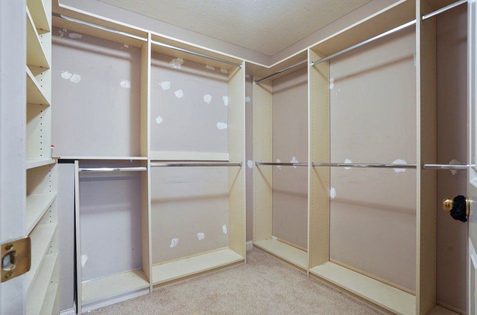 Empty white walk-in closet with shelves, drawers, and hanging rods. Dark wood floor.