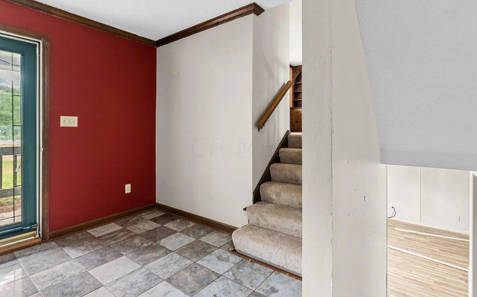 A modern entryway with black door, white mudroom, wood bench, and staircase.
