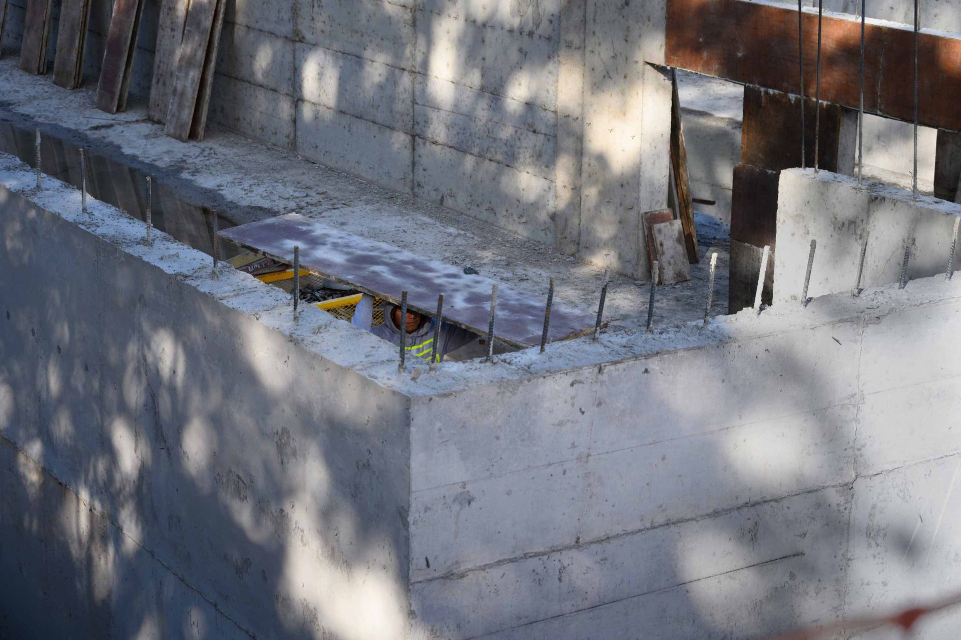 Concrete wall and steps in a sunlit outdoor courtyard with shadows and a metal gate.
