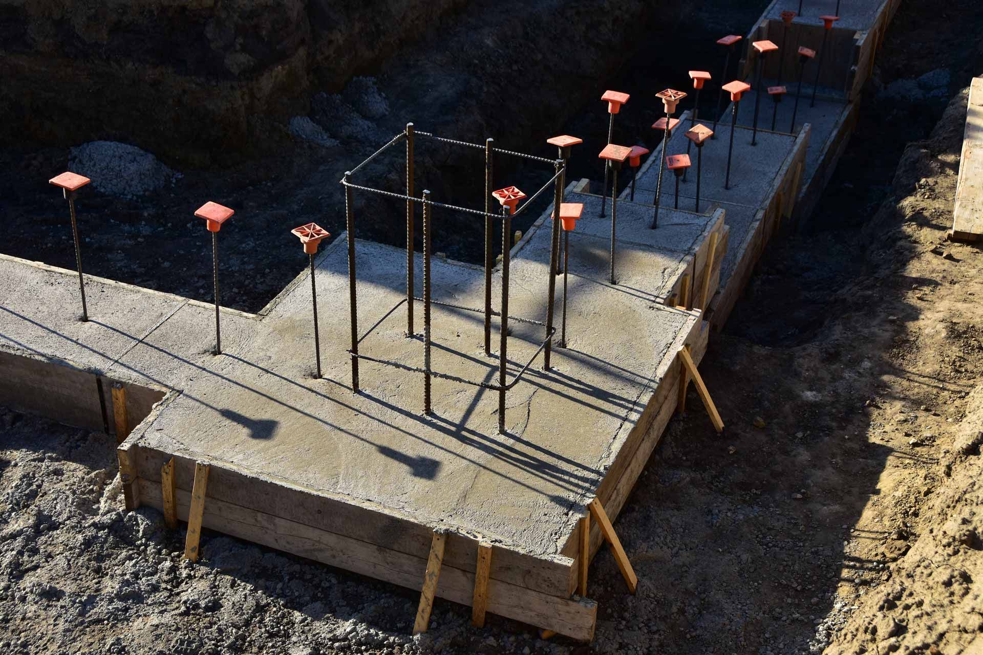 Concrete foundation with rebar and pink marker lights along a construction trench